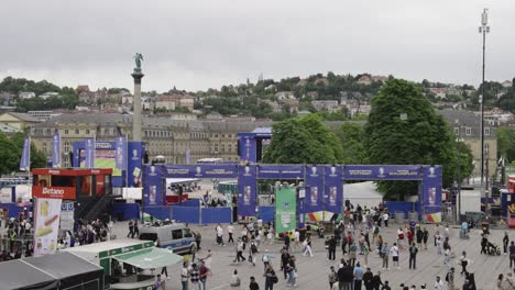 Busy-fanzone-entrance-to-public-viewing,-Jubilee-Column-in-Stuttgart,-Germany-during-Euro-2024-high-wide-static-while-people-are-passing-by-with-copy-space