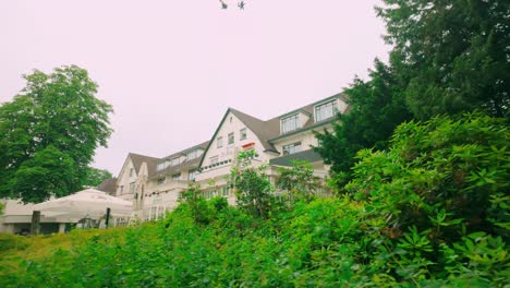 The-famous-facade-of-Hotel-Bilderberg-in-Oosterbeek-is-beautifully-framed-by-green-plants-during-spring,-showcasing-the-hotel's-charming-and-picturesque-setting