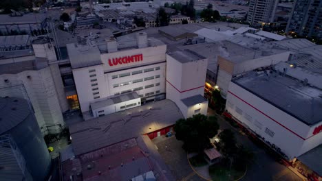 Aerial-view-around-the-illuminated-Lucchetti-factory,-night-in-Santiago-de-Chile