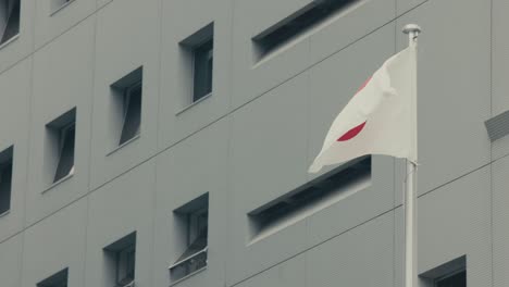 Flag-Of-Japan-On-Flagpole-Against-Building-In-Osaka,-Japan