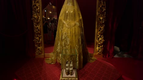 Escaparate-De-Un-Vestido-Dorado-De-Alta-Costura-Con-Diseños-Intrincados-Exhibido-En-Una-Exposición-De-Alta-Costura,-Con-Zapatos-Elegantes