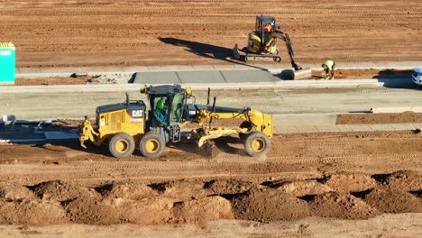 Vista-Aérea-Cercana-De-Una-Niveladora-Y-Otros-Equipos-Pesados-Trabajando-En-Un-Nuevo-Sitio-De-Construcción-Residencial