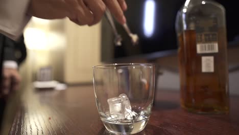 Hombre-De-Traje-Poniendo-Cubitos-De-Hielo-En-Un-Vaso-Preparándose-Para-El-Whisky.