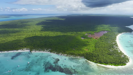 Slight-overhead-drone-shot-above-a-beachfront-in-the-Dominican-Republic,-showing-some-nearby-islands-and-the-forested-areas-in-the-Caribbean-archipelago