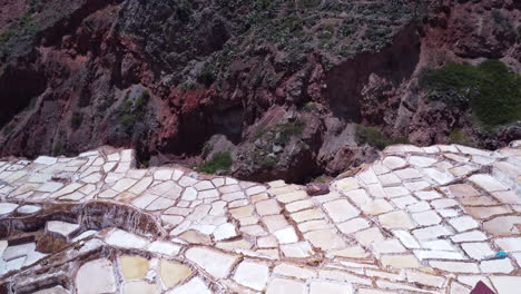 Salt-Mines-of-Maras-in-the-Sacred-Valley-of-Peru,-slow-aerial-dolly-over-drop-off-to-rocks