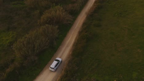 Aerial-view-tilting-over-a-car-driving-on-the-coast-of-Magoito,-sunset-in-Portugal