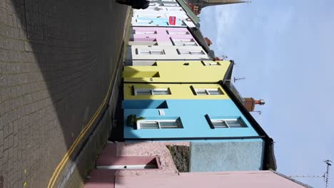 Vertical-panning-left-shot-of-a-hidden-street-in-Tenby,-featuring-colorful-houses-with-a-church-in-background