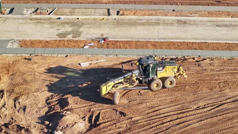 Vista-Aérea-Cercana-De-Una-Niveladora-Trabajando-Y-Dando-Vuelta-Para-Otra-Carrera-En-Un-Sitio-De-Construcción