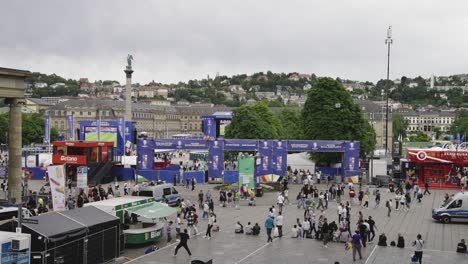 Busy-fanzone-entrance-to-the-Schlossplatz,-Jubilee-Column-in-Stuttgart,-Germany-during-Euro-2024-with-a-stage-in-the-foreground-and-hills-and-green-trees-in-the-background,-static