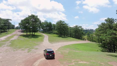 Una-Vista-Aérea-Captura-Un-Todoterreno-Negro-Que-Conduce-Cuesta-Arriba-Por-Una-Carretera-Sinuosa-Rodeada-Por-Un-Denso-Bosque-De-Pinos