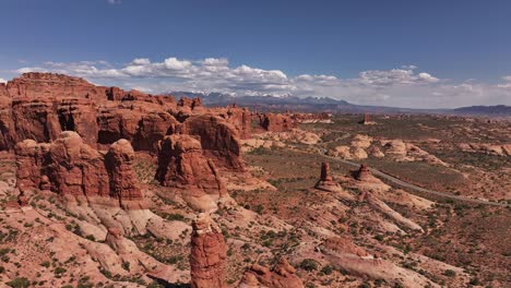 Drone-view-of-red-rock-formations-in-Moab,-USA,-with-cars-traveling-on-a-scenic-road-during-summer