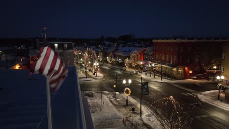 Proud-american-flag-waving-in-front-of-christmas-decorated-street-at-night