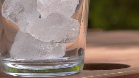 Close-Up-of-Textured-Ice-Cubes-Falling-into-Clear-Clean-Glass-on-Picnic-Table-During-Summer---4K-Slow-Motion-Footage