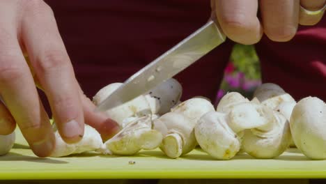 Man-Hands-Cutting-Fresh-Organic-Baby-Button-Mushrooms-on-Chopping-Board-Outside---4K-Slow-Motion-Clip