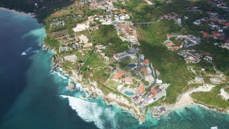 Toma-Aérea-Panorámica-De-La-Playa-De-Uluwatu,-Badung,-Bali-Con-Clubes-De-Playa,-Complejos-Turísticos-Y-Bienes-Raíces-Ubicados-En-La-Cima-Del-Acantilado.