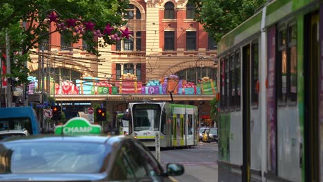 Bustling-city-of-Melbourne,-trams-running-along-Elizabeth-Street,-vehicles-traffic,-and-street-decorated-with-festive-decorations-during-Christmas-season,-a-vibrant-urban-street-scene-in-slow-motion