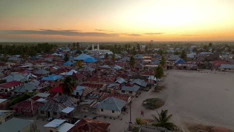 Watch-as-the-drone-flies-toward-Paje's-city-mosque-at-dusk,-with-the-sun-setting-the-sky-ablaze-in-yellow-and-red-hues