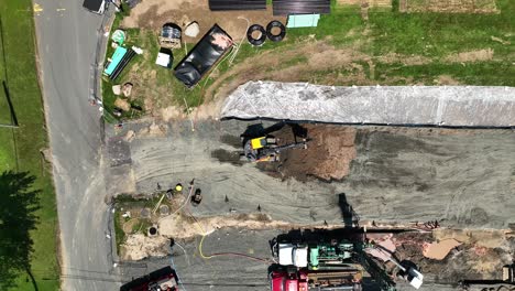 Drone-top-down-rising-above-excavator-and-shadow-in-grassy-field-worksite