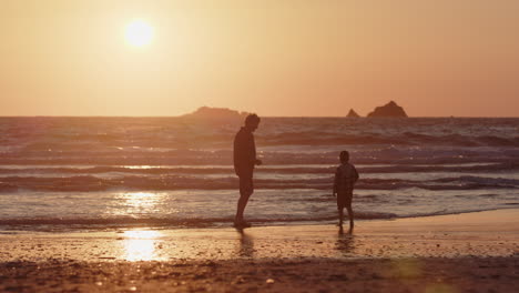 Alleinerziehender-Vater-Bringt-Seinem-Kleinen-Sohn-Bei,-Wie-Man-Bei-Sonnenuntergang-Am-Strand-Steine-übers-Wasser-Hüpfen-Lässt