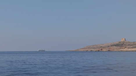 Fernsicht-Auf-Ein-Boot,-Das-Auf-Dem-Meer-In-Der-Nähe-Der-Insel-Comino,-Malta,-Schwimmt,-Mit-Dem-Hohen-Turm-Von-Saint-Mary