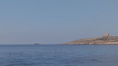 Vista-Lejana-De-Un-Barco-Flotando-En-El-Mar-Cerca-De-La-Isla-De-Comino,-Malta,-Con-La-Torre-De-Santa-María-Erguida