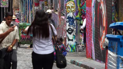 People-walking-through-Hosier-Lane-in-Melbourne-city,-a-cobblestone-laneway-with-a-vibrant-array-of-art-murals-and-graffiti-on-the-walls,-slow-motion-shot-captures-a-creative-cultural-street-scene