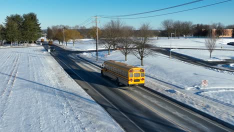 Aerial-tracking-shot-of-several-yellow-school-buses-on-icy-road-during-snowy-winter-day-in-american-suburb