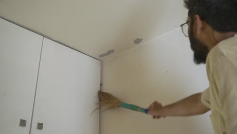 A-South-Asian-man-cleaning-the-house-wall-using-Indian-broomstick-before-the-festival-season-begins