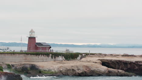 Una-Hermosa-Panorámica-Del-Icónico-Faro-De-Santa-Cruz-Steamer-Lane-Al-Final-De-Un-Acantilado-Rocoso,-Con-Olas-Rompientes-Y-Un-Océano-Azul-En-Primer-Plano