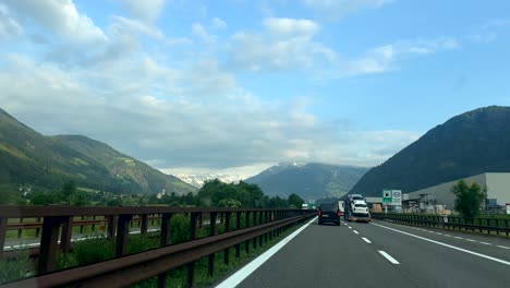 Pov-shot-on-austrian-brenner-highway-showing-traffic-on-road,-green-mountains-landscape-and-snowy-peak-in-summer