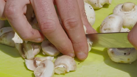 Top-View-of-Organic-Baby-Button-Mushrooms-Being-Cut-into-Small-Pieces-with-Knife-by-Male-Chef-Outside---4K-Slow-Motion-Clip