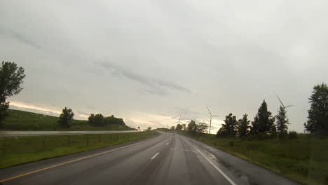 Driving-point-of-view-on-wet-highway-with-windshield-wipers-passing-wind-turbines