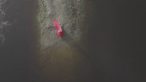 Aerial-drone-shot-of-a-woman-sitting-near-water-and-throwing-a-rock-in-to-the-water