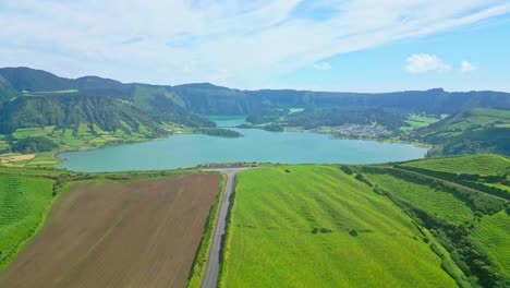 Lush-green-hills-surrounding-a-tranquil-lake-on-a-clear-day,-aerial-view