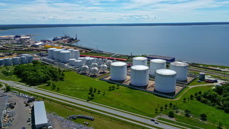 Aerial-drone-backward-moving-shot-over-oil-storage-tanker-depot-along-seaside-in-Paldiski,-Harju-County,-Estonia-on-a-sunny-day