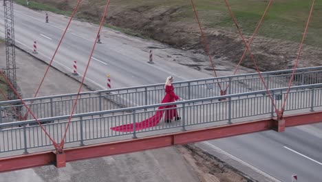 Eine-Drohnenaufnahme-Eines-Models,-Das-In-Einem-Wunderschönen-Roten-Festivalkleid-über-Eine-Brücke-Geht