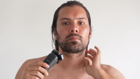 latin-long-hair-man-shaving-with-electric-shaver-in-bathroom,-stylish