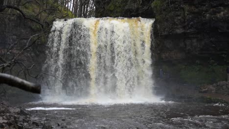 Close-up-shot-of-stunning-Sgwd-Yr-Eira-Waterfall-with-people-walking-behind-it