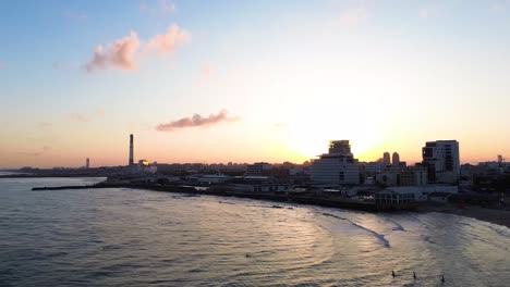 Sonnenaufgang-über-Der-Küstenskyline-Von-Tel-Aviv-Mit-Menschen-Im-Wasser-Am-Metzitzim-Strand