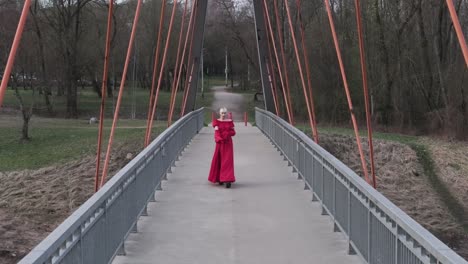 Descending-drone-shot-of-model-wearing-beautiful-dress-and-walking-on-a-bridge