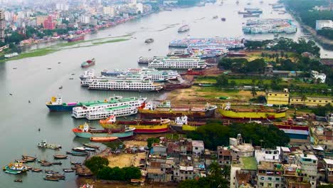 A-bustling-river-port-with-colorful-cargo-ships,-busy-waterway-traffic,-against-an-urban-backdrop,-aerial-view