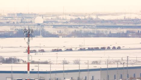 A-snowy-scene-at-an-airport-in-Toronto,-Canada,-featuring-a-line-of-snowplows-clearing-the-runway