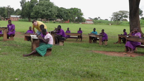 African-children-studying-outdoors-in-a-rural-area-with-a-caucasian-teacher-walking-by-and-checking-their-work