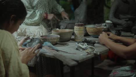 Women-shaping-clay-at-a-pottery-workshop-table-filled-with-tools-and-bowls