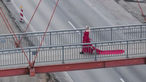 Birdseye-shot-of-a-model-in-red-dress-walking-and-posing-on-a-concrete-bridge