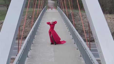 Slow-moving-aerial-drone-shot-of-a-beautiful-model-wearing-fashion-dress-on-a-bridge