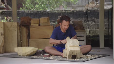 Carver-asian-man-hand-crafting-wooden-sculpture-sitting-in-the-floor