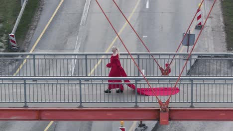 Aerial-shot-of-a-person-walking-with-vibrant-red-dress-walking-across-the-bridge