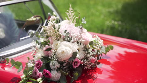 Beautiful-wedding-bouquet-with-pink-and-white-flowers-on-the-hood-of-a-red-vintage-car,-capturing-elegance-and-romance-in-a-classic-setting