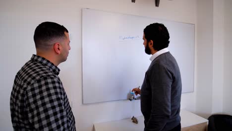 Two-men-writing-and-discussing-at-a-whiteboard-in-a-modern-office-environment